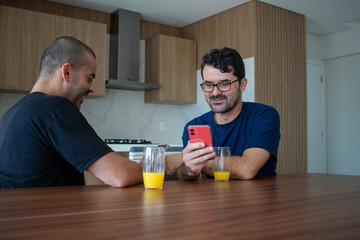 gay men couple relaxed in their apartment drinking orange juice researching their next trip
