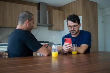 gay men couple relaxed in their apartment drinking orange juice researching their next trip
