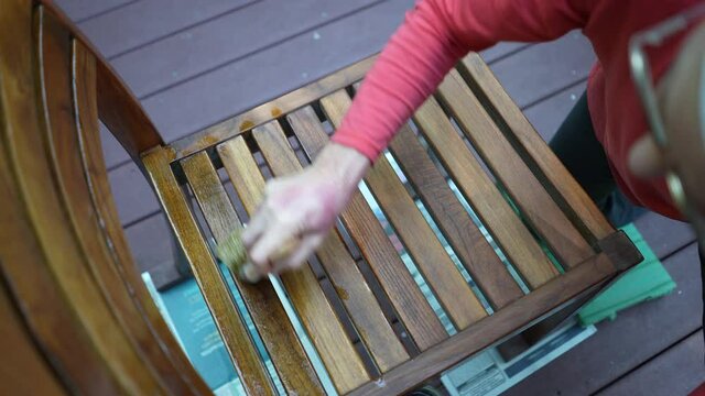 Overhead view of mature woman applying varnish to teak table furniture in garden area at home.