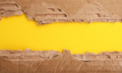 A piece of brown torn corrugated cardboard on a yellow background.Space for text. 