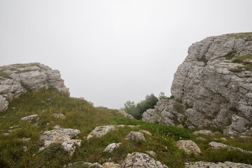 Stony slopes of the Ai-Petri mountain in dense fog. The slope is overgrown with grass.