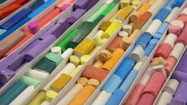 Multi-colored crayons of the various types, shapes and sizes lay out in separate cells in a box for storing crayons. Turntable, background