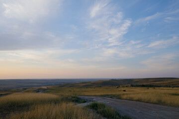 Peaks of hills with steppe grass. Sunset sky and feather clouds.