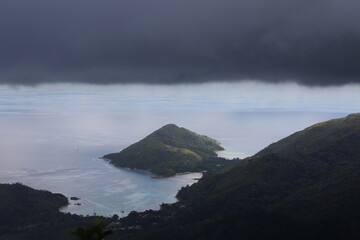Black clouds over the mountains on the coastline and the sea.Stormy skies covered the green island and lagoon.Background image of tropical gloomy rainy day aerial view