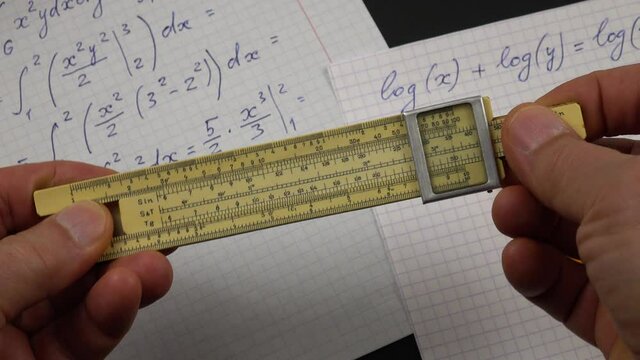 A person makes calculations on a vintage slide rule in the process of performing of the mathematical computations