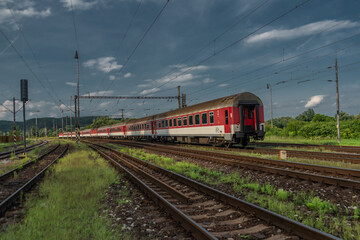 Fototapeta na wymiar Passenger train with red electric locomotive and passenger coaches in summer