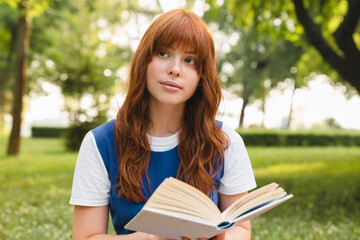 Fototapeta premium Pensive thoughtful young red-head woman teenage girl with ginger hair reading book, literature lover. Caucasian teenager preparing for test exam, doing homework.