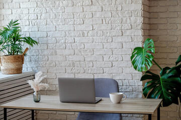 Creative workspace of a blogger. Laptop computer on wooden table in loft style corner office with brick walls and big windows. Designer's table concept. Close up, copy space, background.