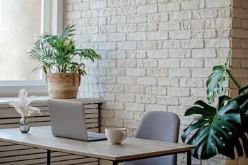 Creative workspace of a blogger. Laptop computer on wooden table in loft style corner office with brick walls and big windows. Designer's table concept. Close up, copy space, background.