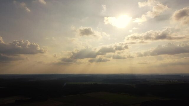 Drone panning over beautiful rural Bavarian landscape against sun with flares and light streaks and cloudy sky