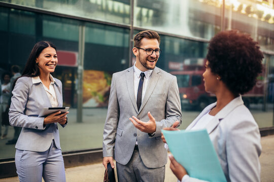 Three Young Business People Talking To Each Other While Walking Outdoors.