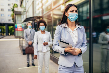 Fototapeta premium Business people with protectiveface mask waiting in line on a safe distance during COVID-19 epidemic.