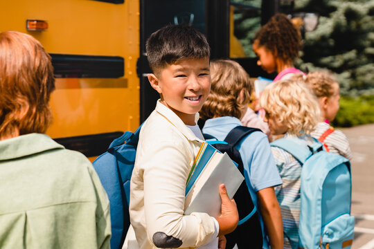 Chinese korean asian schoolboy pupil standing in line with his classmates waiting for boarding school bus preparing for learning lessons new educational year semester.