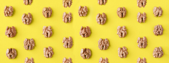 Pattern with halves of walnuts on yellow background, flat lay, banner.