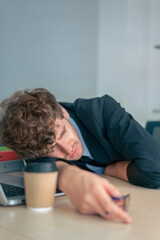 Tired businessman naping at office desk after all day working, with coffee cup.