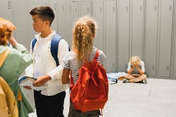 Lonely sad schoolboy crying at the school hall floor while his classmates ignoring him. Bullying at school problem. Social excluding concept - obrazy, fototapety, plakaty
