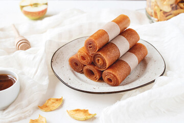 Raw apple pastille rolls, marshmallow with honey on ceramic kitchen board and white tablecloth.