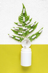 Vitamin supplements and medicines in a bottle and scattered in fern leaves on a green background