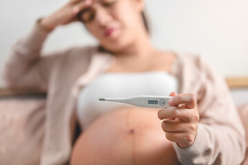 Pregnant asian woman used digital thermometer on bed at morning, Sick female with high fever, Selective focus, Healthy and infection,
