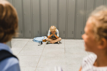 Bullying at school between teenagers. Lonely sad boy crying sitting on the school floor. Torturing,...