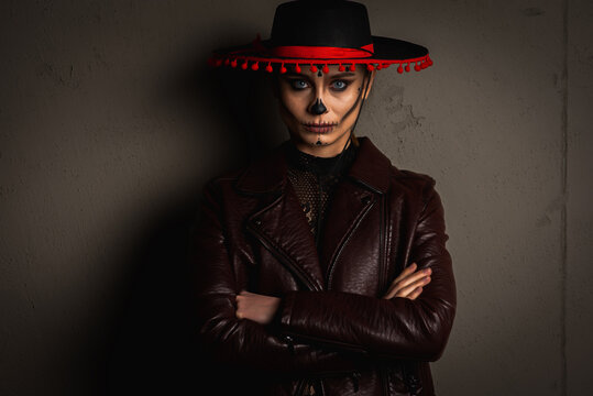 portrait of Kalavera Katrina. Sugar skull makeup in a hat on a gray background looks straight, arms crossed. Dia-de -los -muertos. Day of the Dead. Halloween.