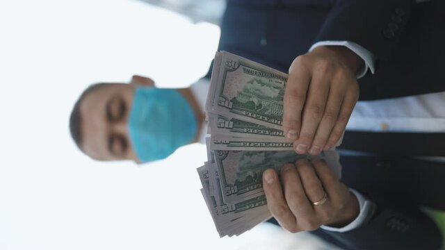 Quarantine financial crisis. The masked man counts cash. Young Handsome Rich Man Wearing Stylish Suit Counting Money Standing in the street near Office Building Vertical Video