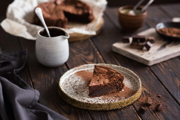 Chocolate cake on a wooden table. A piece of brownie on a brown background. Cocoa and chocolate pieces. Serving dessert.