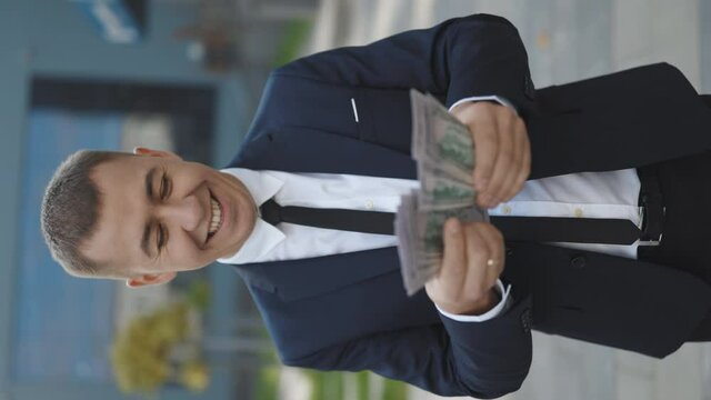 Young Handsome Rich Man Wearing Stylish Suit Counting Money Standing in the street near Office Building Vertical Video. Happy good looking man in business style holding dollars and calculating