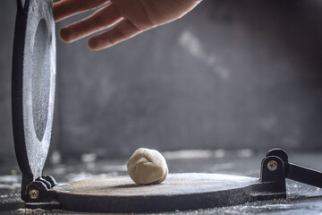 Preparing Dough for Mexican corn tortillas for tacos with tortilla press on grey table top. Closing the press