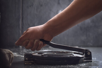 Preparing Dough for Mexican corn tortillas for tacos with tortilla press on grey table top. Closing the press