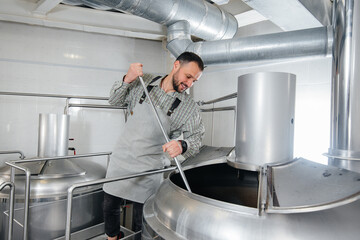 A young male brewer is engaged in the brewing process in a small brewery. Beer production.
