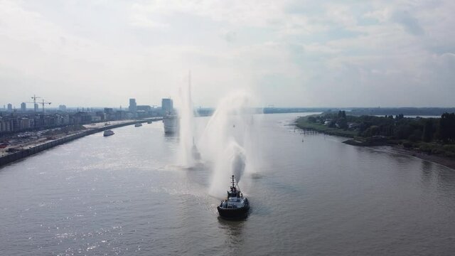 Aerial video of tugboat spraying water and spinning circles on the river Scheldt in Antwerp to welcome the medial ship Mercyships