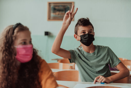 The boy is sitting in a school desk and wearing a mask on his face against corona virus protection. New normal. Education during the Covid-19 pandemic. Selective focus.