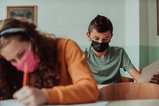 The boy is sitting in a school desk and wearing a mask on his face against corona virus protection. New normal. Education during the Covid-19 pandemic. Selective focus. - Powered by Adobe
