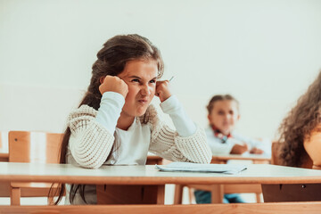 An angry face of a little girl sitting in a school desk.Selective focus