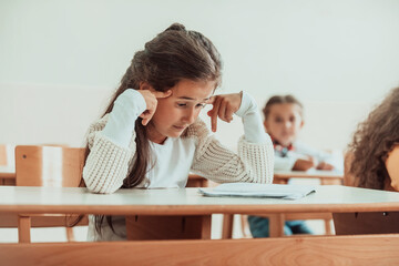 The girl sitting confusedly with her hands on her head in the school desk and attends classes....