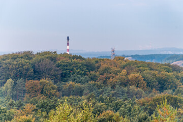 Fototapeta na wymiar Mine shaft tower and factory chimney emerging form trees peaks, lightened by rising sun. Aerial view on autumn forest. Forest, factory and mining heap in the background. Katowice, Silesia, Poland.