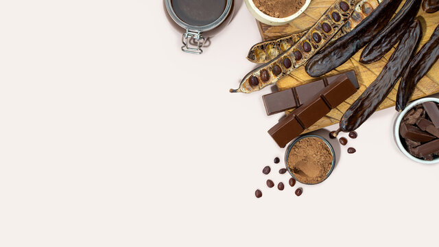 Organic carob pods, powder and carob molasses on a beige background, locust bean healthy food, Ceratonia siliqua harnup. Natural vegan eating. creative food background. Copy space.Flat lay.Top view