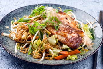 Traditional Japanese fish teriyaki with yakisoba noodles and vegetable served as close-up on a...