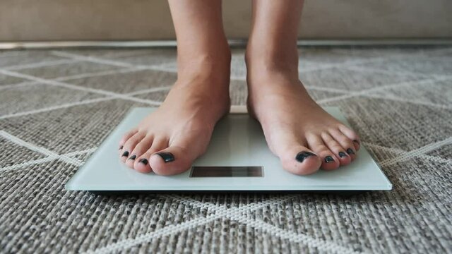 Weighing on scales, woman legs standing on scales standing on floor at home