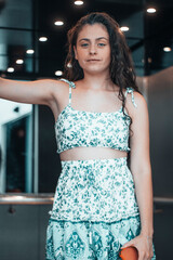 Muchacha joven de pelo rizado oscuro posando con una sonrisa en el ascensor de una empresa para acceder a la siguiente planta