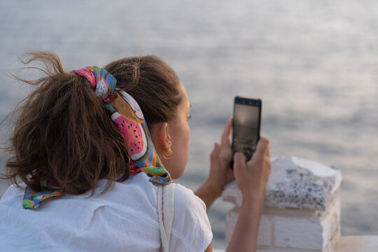 Back view of a woman taking a picture of a sunset with smartphone