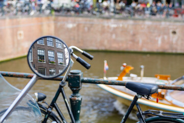 Bicycle mirror reflects windows of building in canal background blurry canal scene