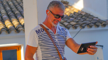 Hombre de mediana edad de vacaciones en Altea con tablet en video conferencia y gafas de sol 