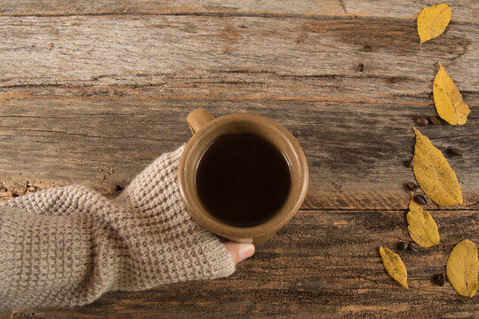 A Sweater Covered Hand Reaching For A Warm Cup Of Black Coffee Over A Rustic, Autumn Table.