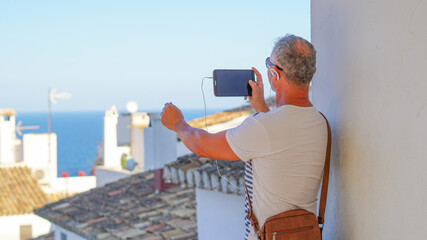 Hombre de mediana edad de vacaciones en Altea con tablet en video conferencia y gafas de sol 