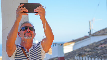 Hombre de mediana edad de vacaciones en Altea con tablet en video conferencia y gafas de sol 