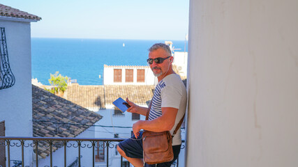 Hombre de mediana edad de vacaciones en Altea con tablet en video conferencia y gafas de sol 