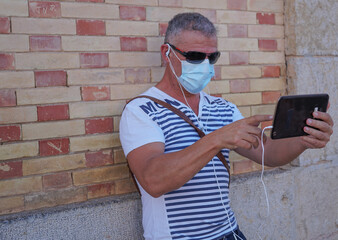 Hombre de mediana edad con mascarilla sanitaria de vacaciones en Altea con Tablet en video...