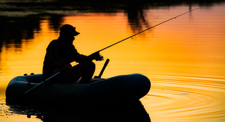 fisherman silhouette in a boat fishing on a lake at sunset